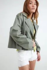 Campera estilo trench corta color beige, con solapas amplias, cierre cruzado de doble botonadura con botones oscuros y diseño holgado.