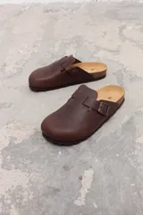 Zueco de cuero marrón con diseño de punta redonda, ajuste mediante correa con hebilla metálica y plantilla de corcho.