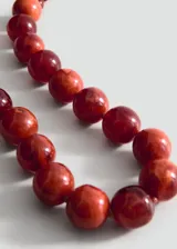 Collar corto de cuentas esféricas grandes en tonos rojizos marmoleados, con cierre de cadena metálica y mosquetón.