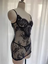 Babydoll de encaje negro semitransparente con diseño floral, tirantes finos regulables, escote con costura de realce y espalda descubierta. Incluye una tanga a juego.