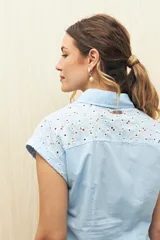 Camisa de manga corta color negro confeccionada en broderie calado, con cuello clásico, cierre frontal de botones y lazo ajustable en la cintura.