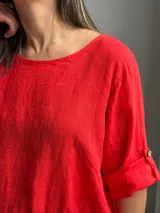 Blusa roja de lino, con cuello redondo, mangas 3/4 con presilla y botones, y diseño holgado con pliegues frontales.