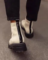 Botas de caña corta color beige, confeccionadas en cuero con textura granulada. Presentan cierre frontal central, suela track negra de goma con costuras blancas visibles y tirador en la parte trasera.