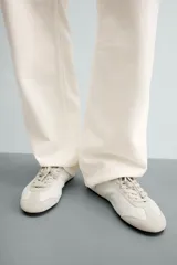 Zapatillas de cuero color blanco roto, de diseño minimalista con cordones, suela fina de goma marrón y detalles de gamuza en la puntera y los ojales.