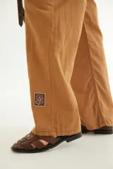 Pantalón de corte recto y tiro medio con costuras a la vista, bolsillos delanteros y traseros, y un detalle de pin de la marca en el ruedo.