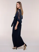 Vestido largo azul marino de seda fría, compuesto por una falda recta con tajo frontal y una capa superior superpuesta de encaje con lentejuelas bordadas, escote a la base y mangas tres cuartos acampanadas.