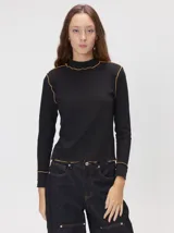 Polera de cuello alto confeccionada en tela rib color negro, con mangas largas y hombreras. Presenta pespuntes en contraste de color en las terminaciones del cuello, sisas, puños y ruedo.
