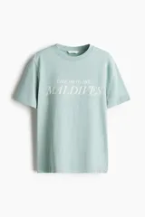Remera de algodón color verde menta, de corte holgado con hombros caídos y cuello redondo acanalado. Presenta un estampado frontal con la frase 'TAKE ME TO THE MALDIVES' en color blanco.