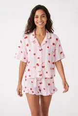 Pijama compuesto por una camisa de manga corta con solapas y botones frontales, y un short con detalles de volados en las piernas. Presenta un estampado de rayas verticales rosadas y blancas con motivos de cerezas.