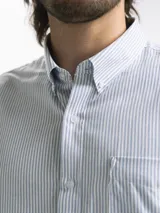 Camisa celeste y blanca a cuadros con cuello abotonado, manga larga y bolsillo en el pecho.