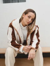 Campera con capucha, de tela tipo peluche a rayas verticales color marrón y blanco, con ribete color beige.