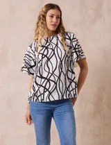 Blusa blanca estampada con líneas y lunares negros, de crepe marca Alex & Parker. Tiene cuello a la base, escote en V con botón y mangas cortas amplias.