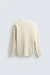 Remera de manga larga de corte regular fit, confeccionada en tejido acanalado con mezcla de algodón y efecto lavado. Cuenta con cuello redondo y cierre frontal corto con tres botones.