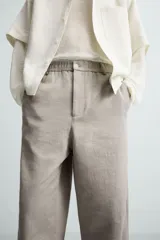Pantalón de vestir color blanco hueso, de corte recto y tiro medio, con cintura elástica y cierre frontal de botón y cremallera. Presenta bolsillos frontales y bolsillos traseros de vivo.