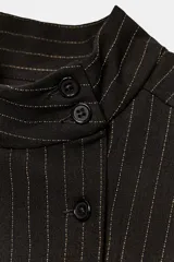 Top de cuello subido y manga muy corta abullonada, de color marrón oscuro con diseño de rayas finas verticales. Presenta doble botonadura frontal y corte entallado.