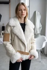 Campera tipo aviador en color crudo, confeccionada en ecocuero con interior y detalles de piel sintética en cuello, puños y ruedo. Presenta cierre frontal cruzado, bolsillos laterales con cierre y un bolsillo tipo cargo en la manga con detalle en cuero sintético, además de una tira ajustable con hebilla en la cintura.
