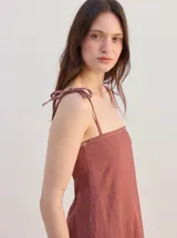 Vestido largo de algodón denim con diseño de rayas verticales en color azul marino y beige. Cuenta con tirantes finos ajustables con lazos en los hombros, escote recto y corte suelto con un volante en el bajo.
