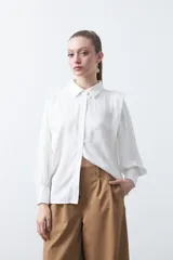 Camisa de estilo sastrero color blanco, con cuello clásico, frente abotonado y mangas largas con puños estructurados y leve volumen en los hombros.