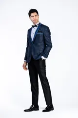 Ambo de ceremonia tipo smoking, compuesto por un saco azul con diseño jacquard y solapa chal de raso al tono, y un pantalón negro satinado de corte slim fit.