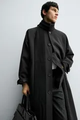 Trench de corte oversized confeccionado en tejido compacto con mezcla de lana. Presenta cuello solapa, cierre frontal con botonadura, mangas largas y bolsillos de vivo en la cadera.