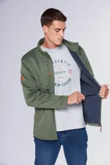 Campera deportiva de tejido tipo polar en color gris jaspeado, con cuello alto, cierre frontal completo, bolsillos laterales y bolsillo en el pecho con cierre. Presenta detalles en cuero sintético y logo bordado en el pecho.