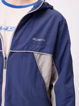 Rompevientos Rusty con capucha, diseño bicolor en azul marino y gris, cierre frontal y logo bordado en el pecho.