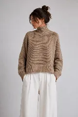 Sweater tejido de punto color blanco, con cuello alto tipo media polera, mangas largas y dobladillo asimétrico con aberturas laterales.