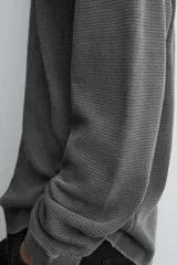 Camiseta de manga larga con cuello redondo, confeccionada en tejido de algodón con textura tipo waffle y efecto lavado. Presenta un corte relajado con puños en rib y bajo irregular.
