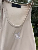 Musculosa de viscosa color beige con diseño acanalado, escote redondo y detalle de bordado en forma de mariposa en el centro del pecho.