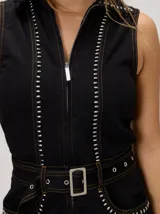 Enterito sin mangas confeccionado en denim de algodón color beige, de fit holgado con pierna recta y tronco entallado. Posee cierre frontal completo, cuello camisero y detalles de tachas metálicas en las costuras. Incluye un cinturón ajustable del mismo material con hebilla rectangular.