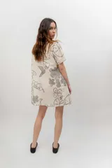 Vestido corto beige con estampado botánico en negro, cuello camisero, mangas cortas y cierre frontal con botones.