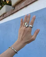 Anillo de diseño orgánico y macizo con forma irregular, elaborado en metal con acabado brillante. Presenta una estructura abierta que permite su ajuste.