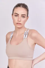 Top deportivo color beige con espalda cruzada, elástico en la base y tiras regulables con logo de la marca.