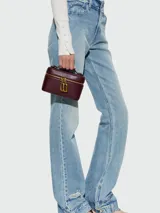 Cartera tipo vanity bag Marc Jacobs modelo The Pop J Marc E/W, color bordó, de diseño estructurado con cierre perimetral de cremallera dorada y herraje metálico distintivo de la marca en la parte frontal. Cuenta con asa superior corta.