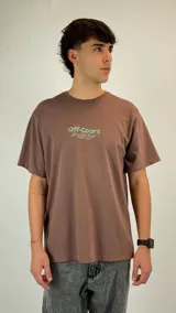 Remera de algodón color marrón con cuello redondo y estampa frontal con texto en tonos verdes.