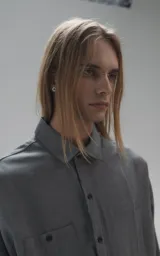 Camisa de manga larga en tejido twill color gris melange, con corte oversize. Presenta cuello clásico, cierre frontal con botones y tres bolsillos delanteros, uno de ellos oculto.