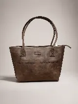 Cartera tipo tote bag de cuero vacuno color marrón oscuro, de diseño estructurado con asas largas para llevar al hombro y cierre superior. Presenta detalles de costuras decorativas y pespuntes en el frente.