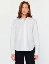 Camisa blanca de manga larga con cuello clásico y cierre frontal de botones. Presenta detalles bordados florales tono sobre tono en la zona de los hombros y el pecho.