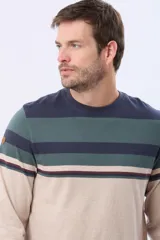 Remera de manga larga con cuello redondo y estampado de rayas horizontales en tonos azul marino, verde oscuro, beige y bordó. Incluye un parche decorativo en la manga izquierda y un pequeño logo bordado en el pecho.