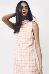 Vestido corto sin mangas de tejido texturizado con diseño de cuadros en tonos crudo y fucsia. Presenta cuello subido, trabillas decorativas con botones dorados en los hombros y cierre lateral con cremallera oculta.
