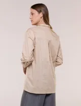 Camisa de silueta holgada y largo extendido, confeccionada en poplín elástico de color blanco. Presenta cuello solapa abierto en V con cartera frontal de abotonadura oculta, hombros caídos y mangas tres cuartos. Cuenta con espalda con canesú, pliegue central y ruedo recto con pequeñas aberturas laterales.