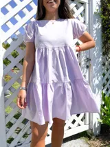 Vestido corto lila de tela tipo camisa, con volados y mangas abullonadas.