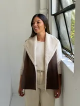 Chaleco de cuero sintético color marrón chocolate con interior y solapas de corderito sintético color crudo. Diseño sin mangas con cierre frontal.