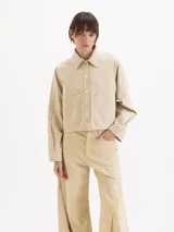 Chaqueta corta de gabardina en color beige, con cuello clásico, cierre frontal con broches metálicos a presión y bolsillos frontales con solapa.