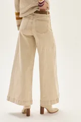 Pantalón de jean color beige claro, tiro alto, de corte ancho (wide leg) y largo hasta el tobillo con dobladillo. Presenta costuras verticales marcadas en el frente de las piernas.