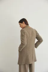 Saco corto entallado de lana fina, con cuello solapa, manga larga y cierre frontal con botones. Presenta un diseño clásico con textura de espiga en tonos tierra.