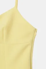 Mono corto amarillo pastel con escote redondo, tirantes finos ajustables y abertura frontal con solapa. Presenta cierre lateral oculto.