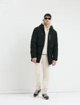 Campera puffer de corte largo, color verde militar, con capucha fija, cierre frontal y puños elásticos internos.