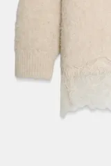 Jersey de punto con cuello barco y manga larga, confeccionado en tejido efecto cepillado. Presenta un diseño asimétrico en el bajo con detalle de encaje aplicado.