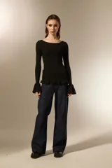 Remera de punto al cuerpo con cuello bote y mangas largas terminadas en volados acampanados. Presenta un ruedo con detalle de volados.